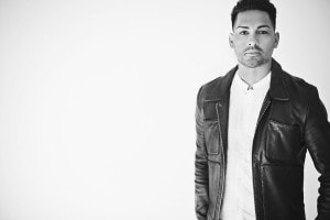 A black and white photo featuring owner and hair artist, Brandon DaSilva, wearing a white button-down shirt with a black leather jacket as he looks directly into the camera.